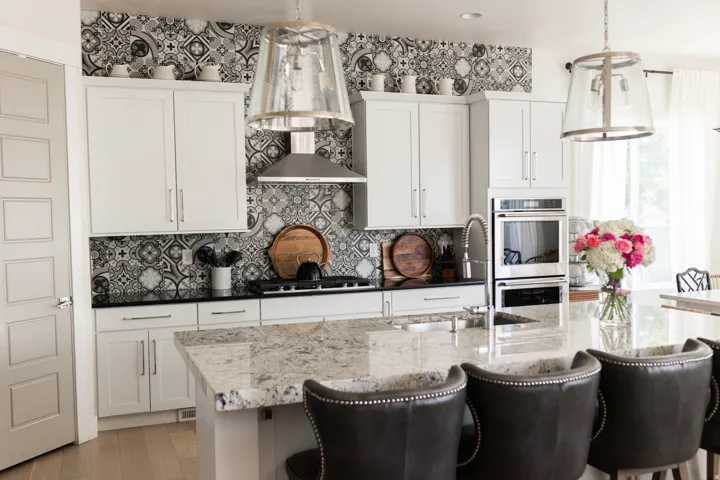 Kitchen featuring a patterned tile backsplash, stainless steel appliances, white cabinetry, a large kitchen island with a stone countertop, and pendant lighting fixtures