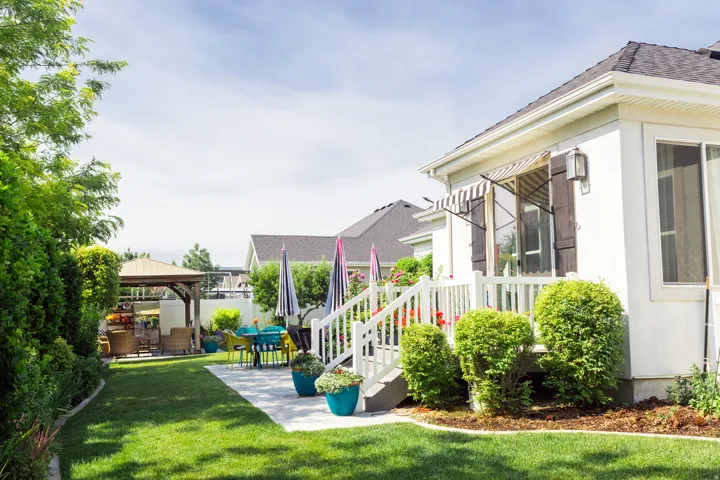 Backyard from north east corner with a white exterior home featuring a striped awning and dark wood shutters