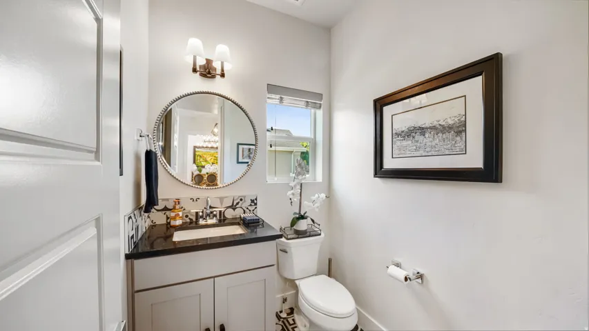 Vanity with dark countertop, round framed mirror, and decorative tile backsplash