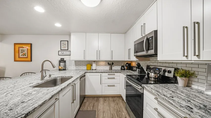Modern kitchen featuring white shaker cabinetry with brushed nickel hardware, light-toned granite countertops, and a subway tile backsplash