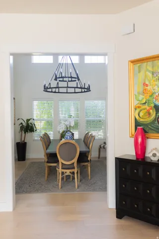 Double-height dining space featuring a large black chandelier, multiple windows with blinds, light wood-finish flooring, and white trim