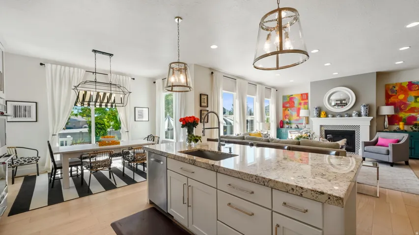 Open-concept kitchen and dining area featuring a large center island with light cabinetry and polished stone countertops, stainless steel appliances, pendant lighting, wood-finish flooring, and expansive windows with natural light