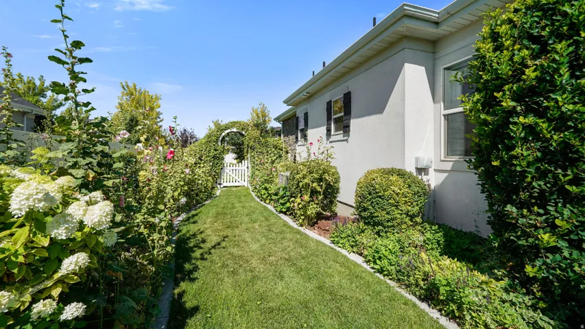 Manicured lawn path leading to a white garden arbor and gate, framed by mature flowering shrubs and foliage