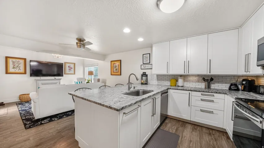 Open-concept kitchen featuring white cabinetry, granite countertops, a subway tile backsplash, and stainless steel appliances