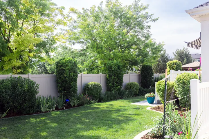 Backyard featuring a manicured lawn, established perimeter landscaping, privacy fencing, a curved concrete patio section, and a garden bed
