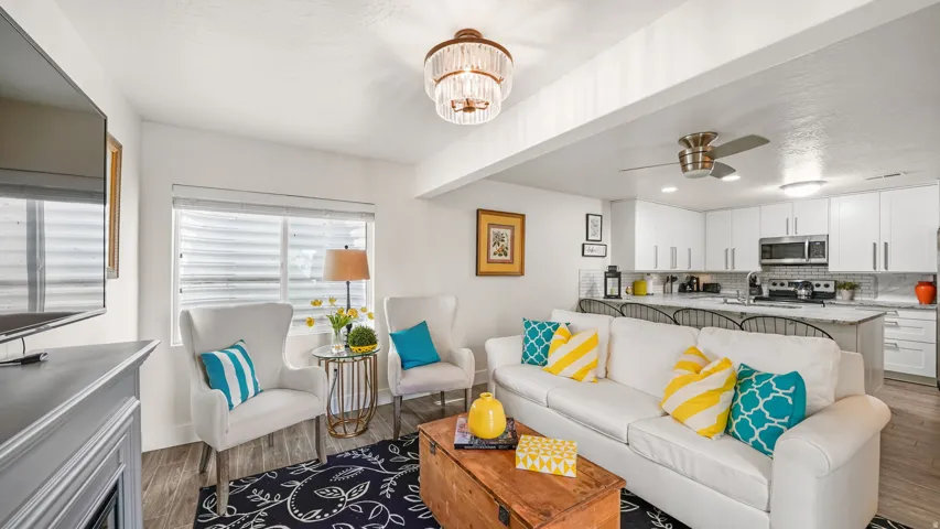 Open-concept living and kitchen featuring a cream upholstered sofa with coordinating accent pillows, wood-finish flooring throughout, and a wood-top coffee table