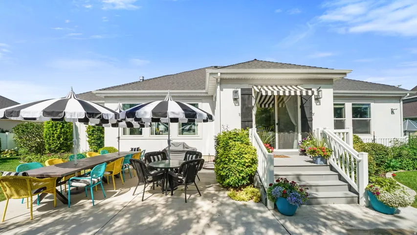 Spacious concrete patio with dual black and white striped umbrellas, a raised entryway with a striped awning, and a manicured lawn
