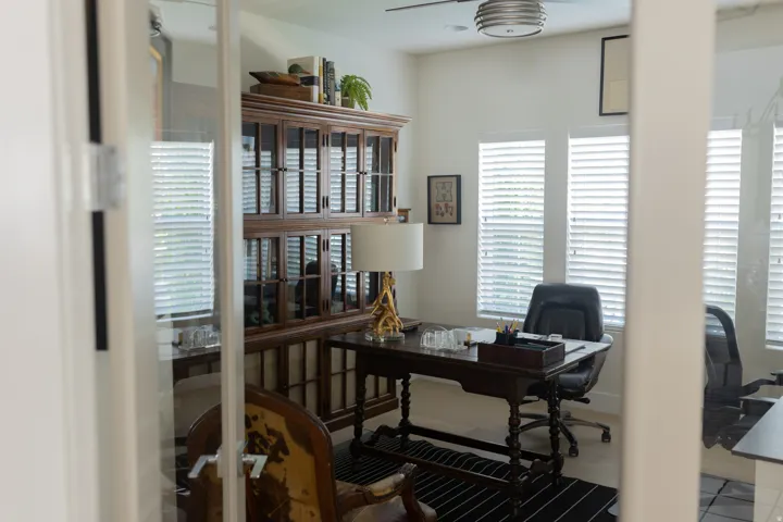 Office space featuring glass French doors, multiple windows with blinds, a ceiling fan, and light-toned flooring