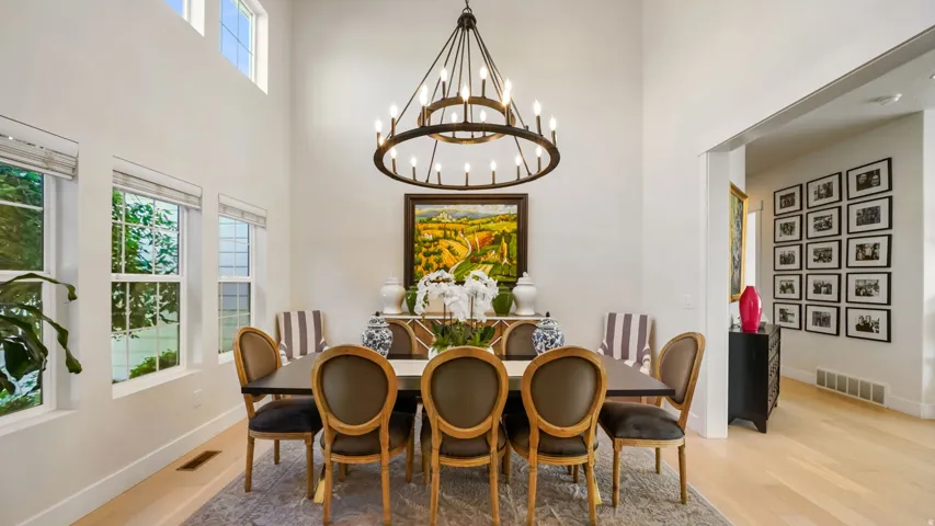 Elegant dining room showcasing a wood-finish plank floor, high ceilings with transom windows, and a statement ring chandelier with bronze-toned metalwork