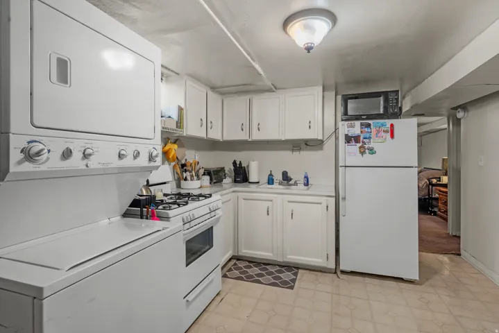 Kitchen area featuring a stackable washer and dryer, gas range, corner sink, and white cabinetry