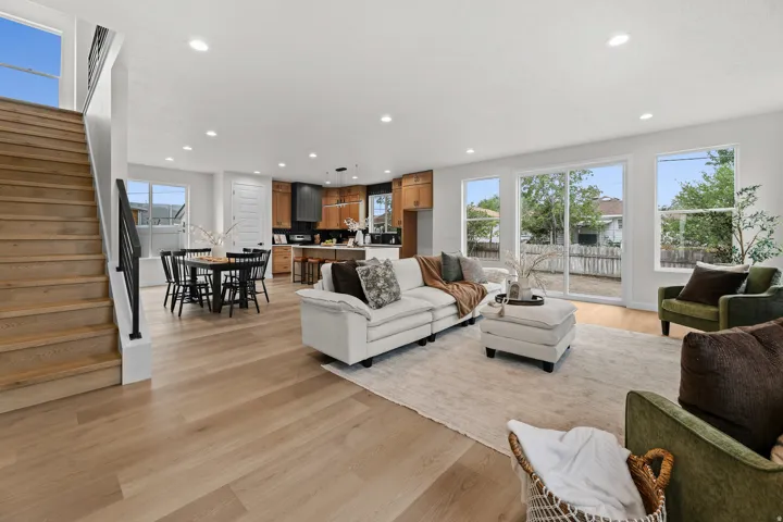 Open-concept living space featuring wood-finish flooring, recessed lighting, and a prominent staircase with a dark metal railing