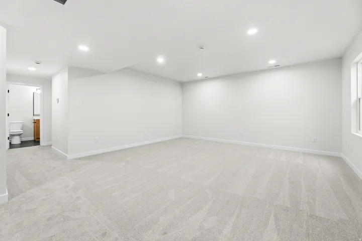 Spacious interior room featuring light-toned carpeting, recessed ceiling lighting, and a white trim baseboard