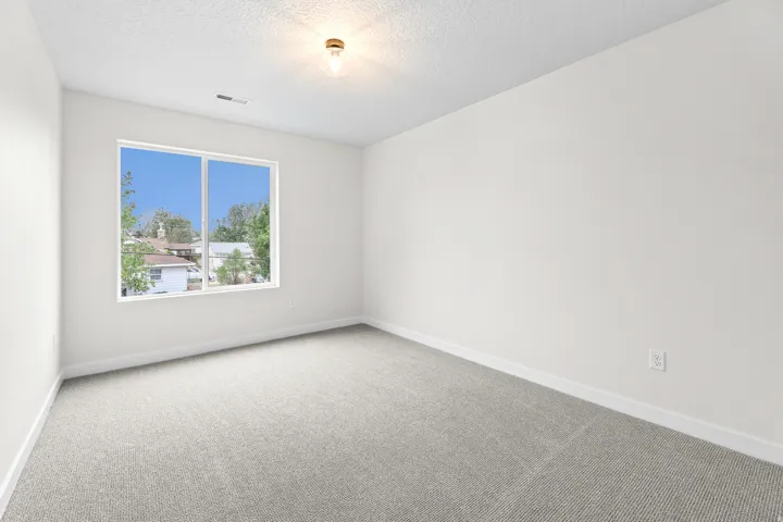 Spacious room with light gray carpeting, crisp white walls, a large window, a ceiling-mounted light fixture, and white baseboards