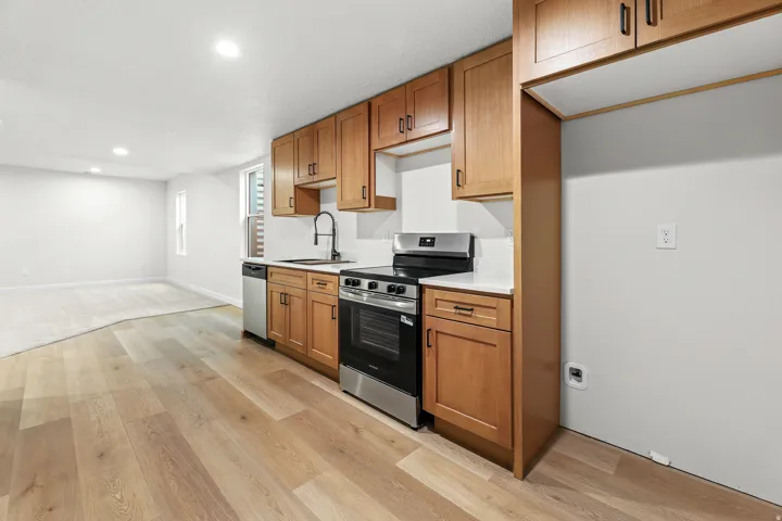 Kitchenette featuring light wood-finish cabinetry, stainless steel appliances, a black gooseneck faucet, and white countertops