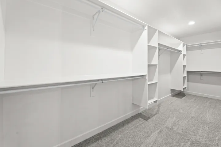 Spacious walk-in closet featuring extensive built-in shelving, multiple hanging rods, and recessed lighting