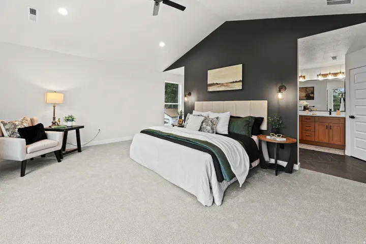 Vaulted ceilings define this space, featuring light gray carpeting, a dark accent wall, recessed lighting, and a ceiling fan
