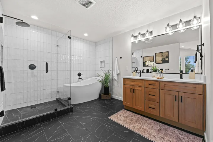 Expansive bathroom featuring dark-toned tile flooring, a freestanding soaking tub, and a walk-in shower with clear glass enclosure