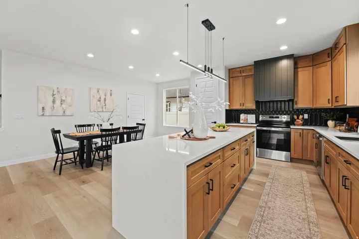 Spacious kitchen featuring a large central island with a white countertop, light wood-finish cabinetry, stainless steel appliances, and a dark tile backsplash