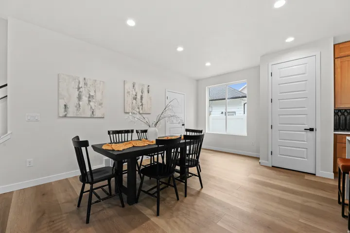 Bright interior space featuring light wood-finish flooring, white walls, recessed ceiling lighting, a large window, and a five-panel interior door with black hardware