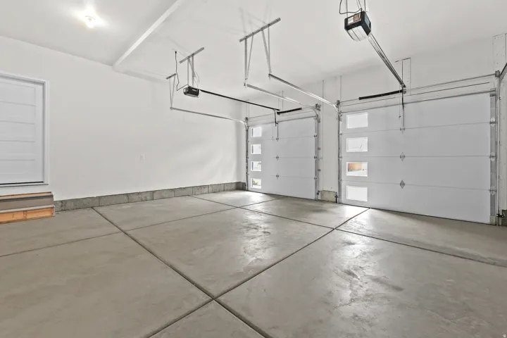 Spacious two-car garage featuring a concrete floor, white walls, and two overhead doors with frosted window inserts