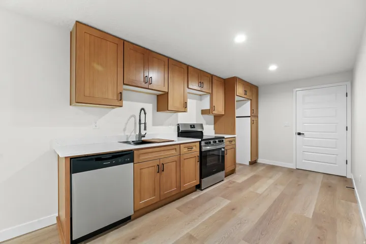 Modern kitchen featuring light wood cabinetry, a stainless steel dishwasher, a stainless steel range, and a black gooseneck faucet
