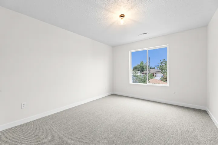 Bright interior space featuring a large window, light-colored walls, textured ceiling, and gray patterned carpeting