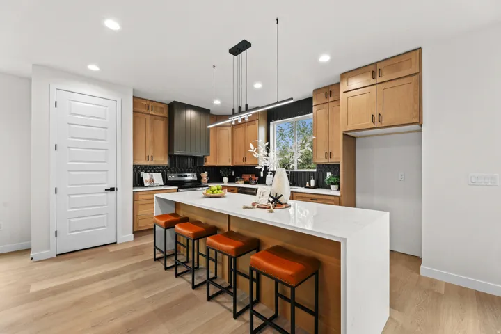 Contemporary kitchen featuring wood-finish cabinetry, a black tile backsplash, and a large center island with a waterfall countertop