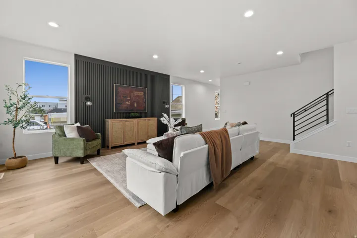 Spacious living area featuring light wood-finish flooring, recessed lighting, and a prominent dark accent wall with vertical paneling