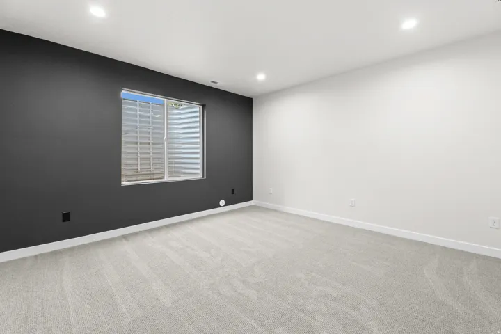 Recessed lighting illuminates a room featuring light-toned carpet, a white ceiling, and contrasting dark gray and white painted walls