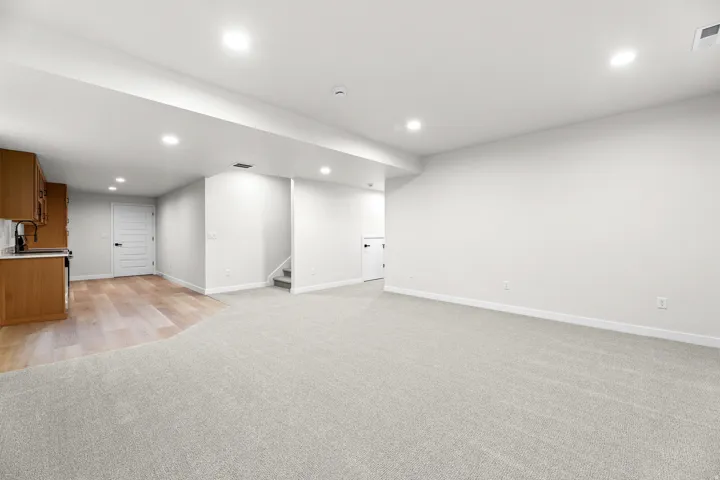 Spacious open-concept room featuring light gray carpeting, recessed ceiling lighting, and crisp white walls