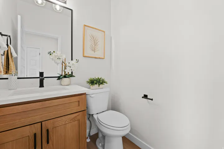 Modern bathroom featuring a wood-finish vanity with a white countertop and integrated sink, matte black faucet, and a contemporary vanity mirror with overhead lighting
