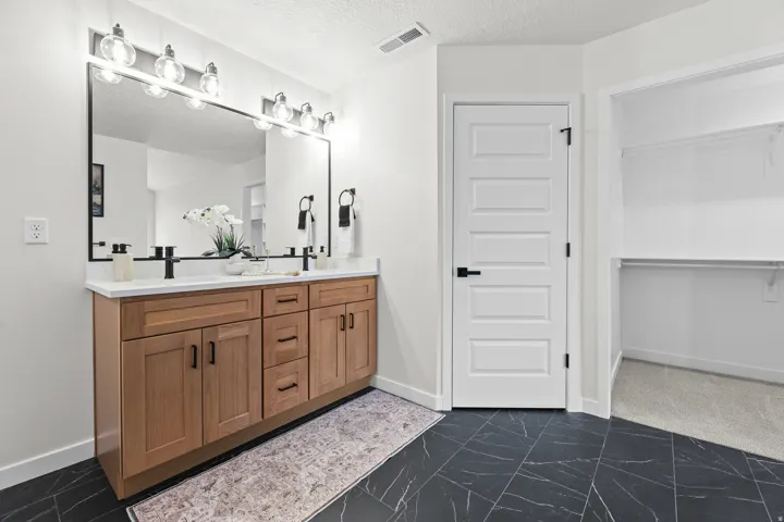 Contemporary bathroom featuring a double vanity with light wood-finish cabinetry, white countertop, and matte black fixtures