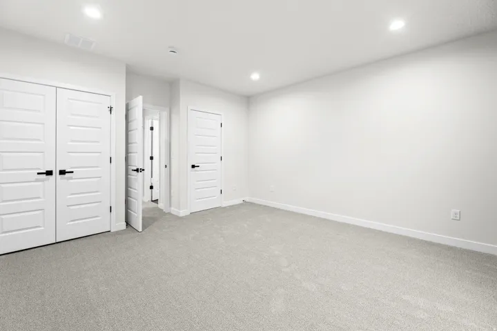 Carpeted interior space featuring recessed lighting, white walls, and multiple paneled doors with black hardware