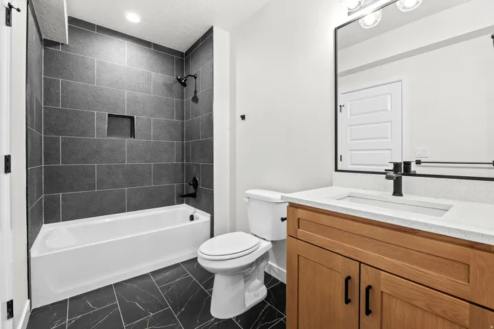 Bathroom featuring a white bathtub with dark gray subway tile surround and a recessed niche