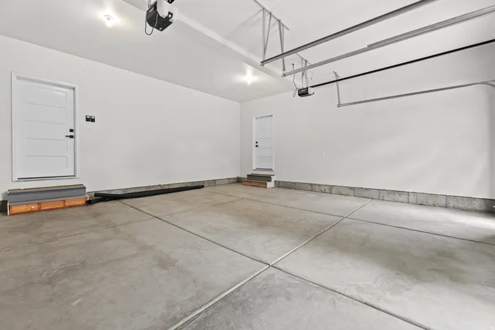 Spacious garage featuring a concrete floor, painted white walls, two entry doors, and overhead garage door track systems