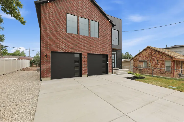 Modern brick and black siding exterior featuring a concrete driveway and two black garage doors with frosted glass panels