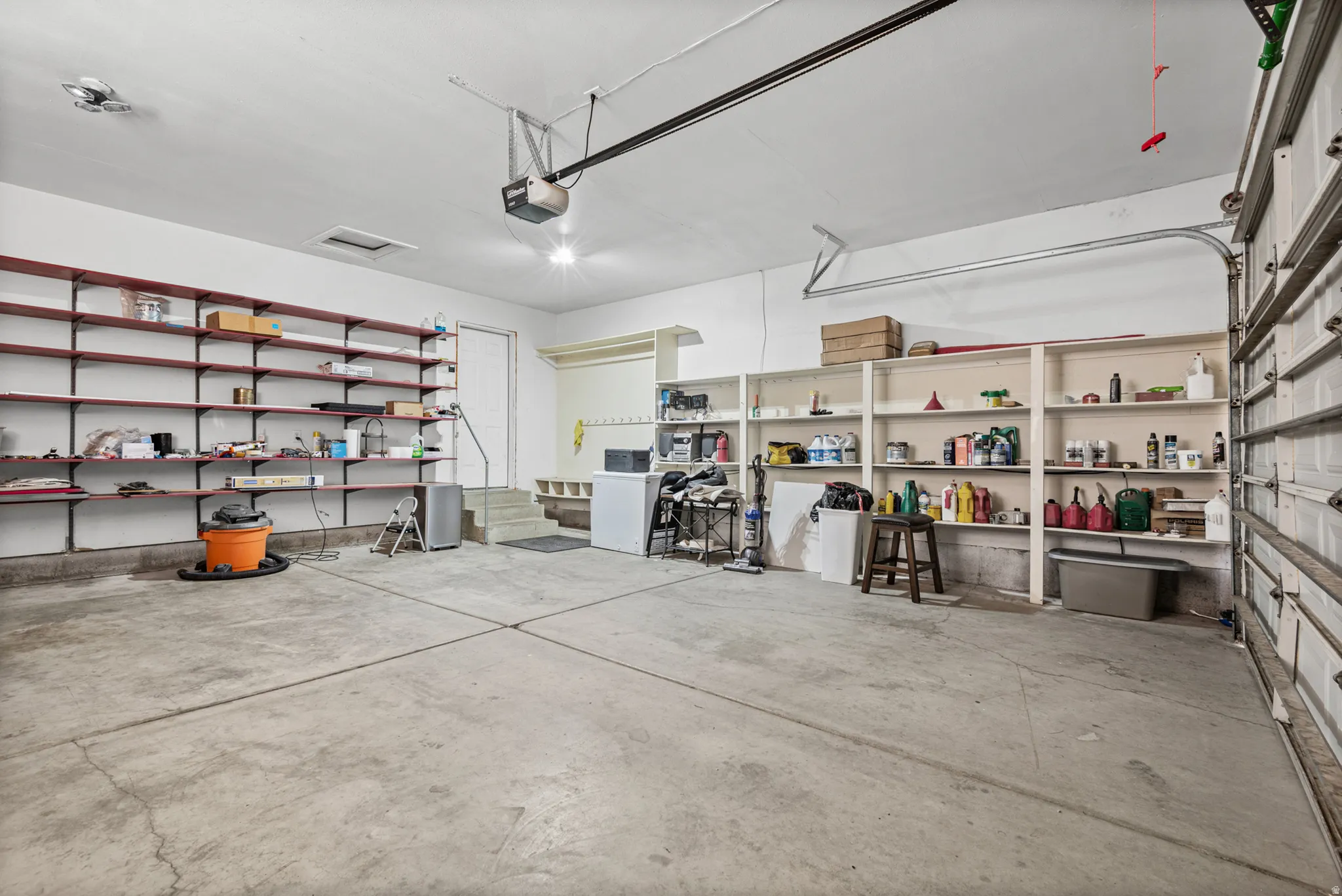 Spacious garage featuring a concrete floor, built-in shelving, overhead lighting, and an automatic garage door opener