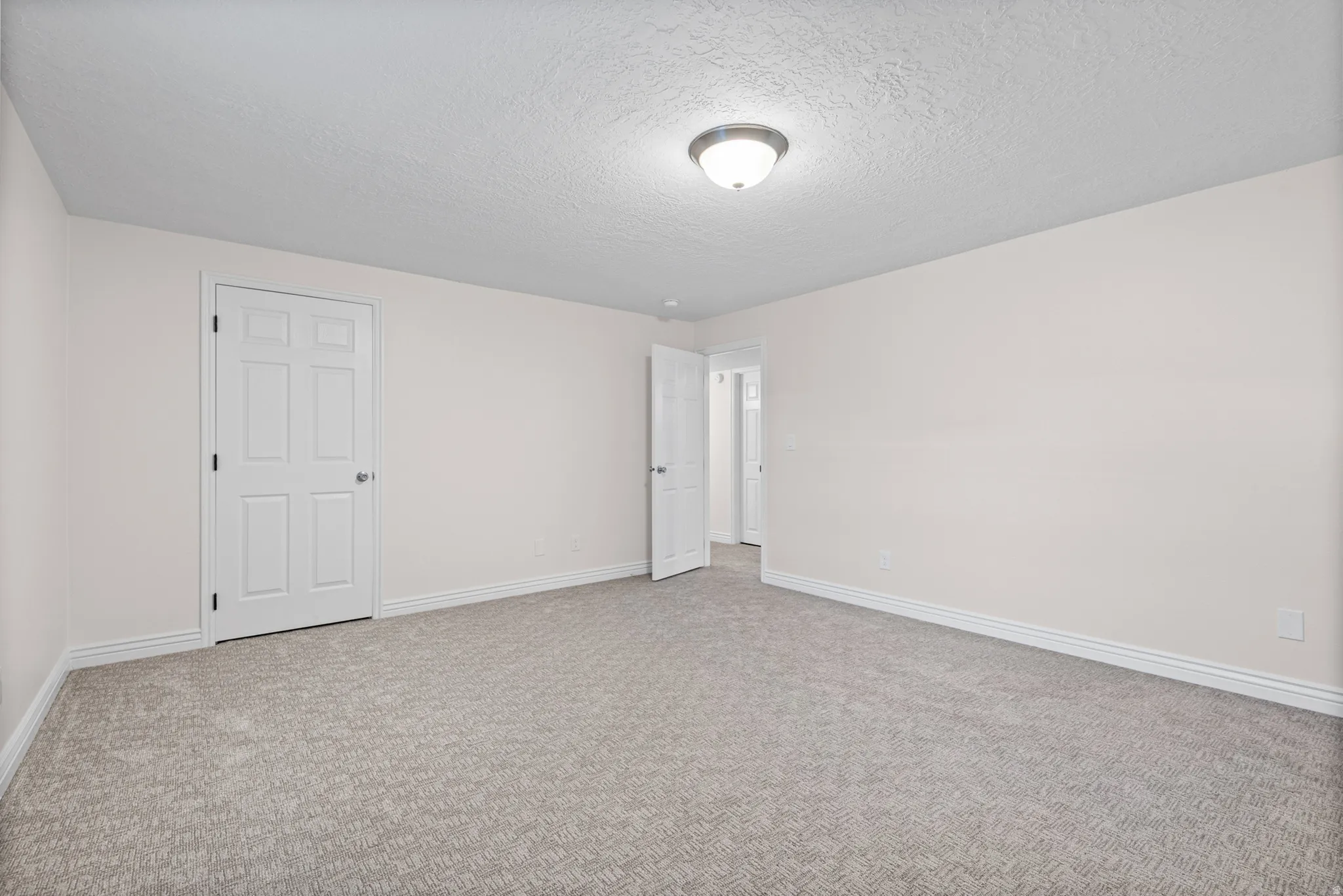 Spacious room featuring neutral carpeting, light-colored walls, white trim, and a semi-flush mount ceiling light fixture