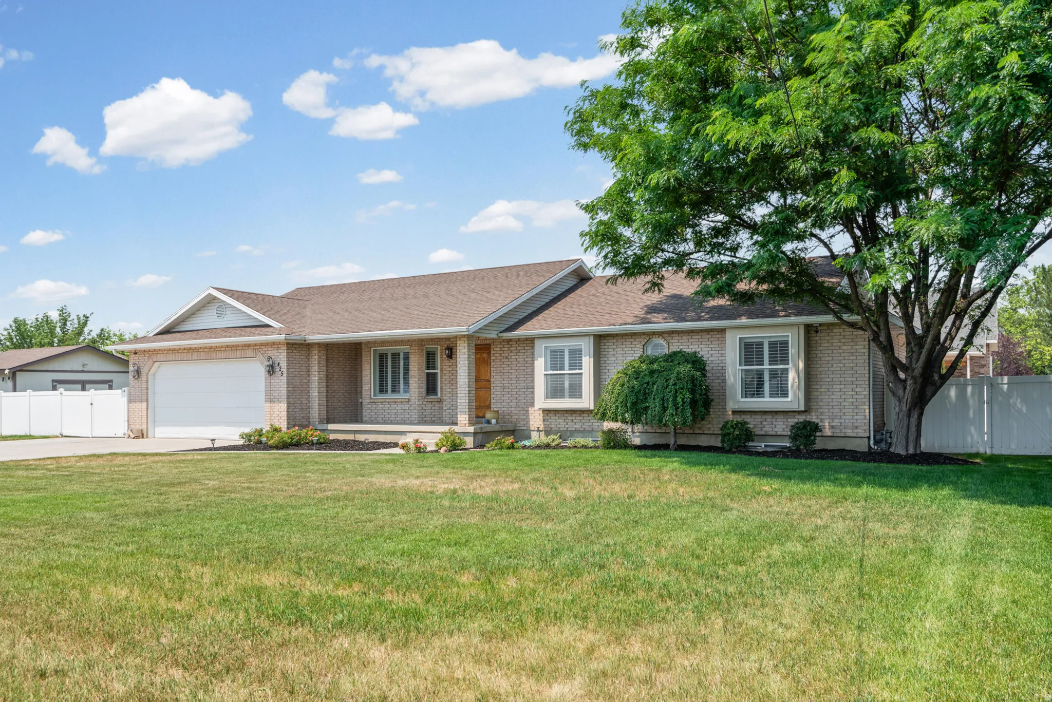 Brick ranch-style exterior featuring a two-car garage, covered porch entry, and a prominent mature tree providing natural shading