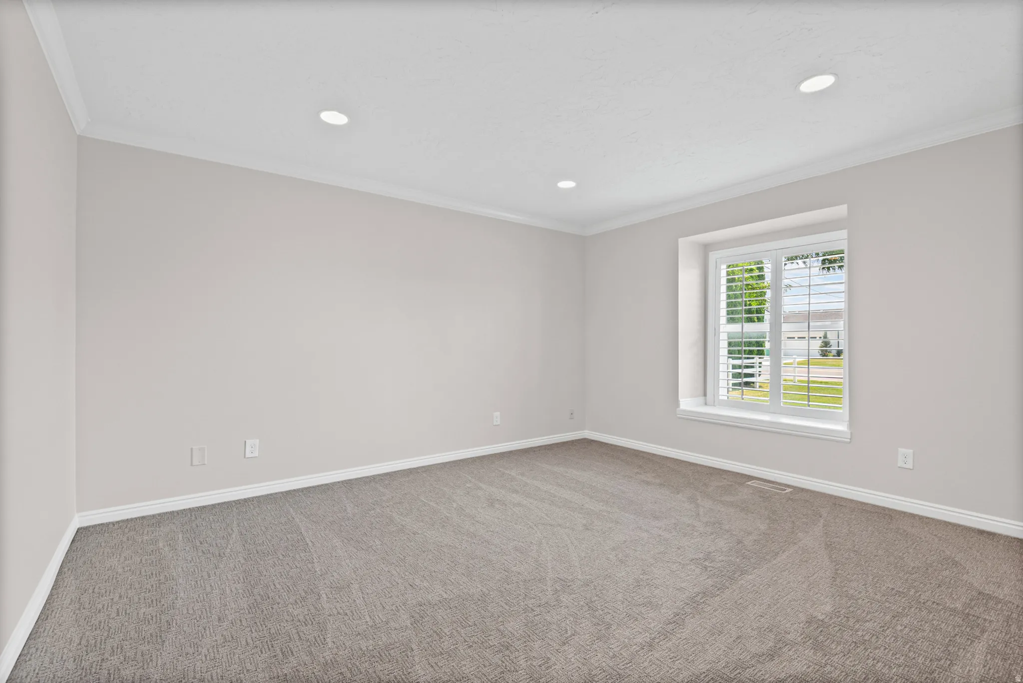 Spacious room featuring neutral carpeting, light-toned walls, and crown molding