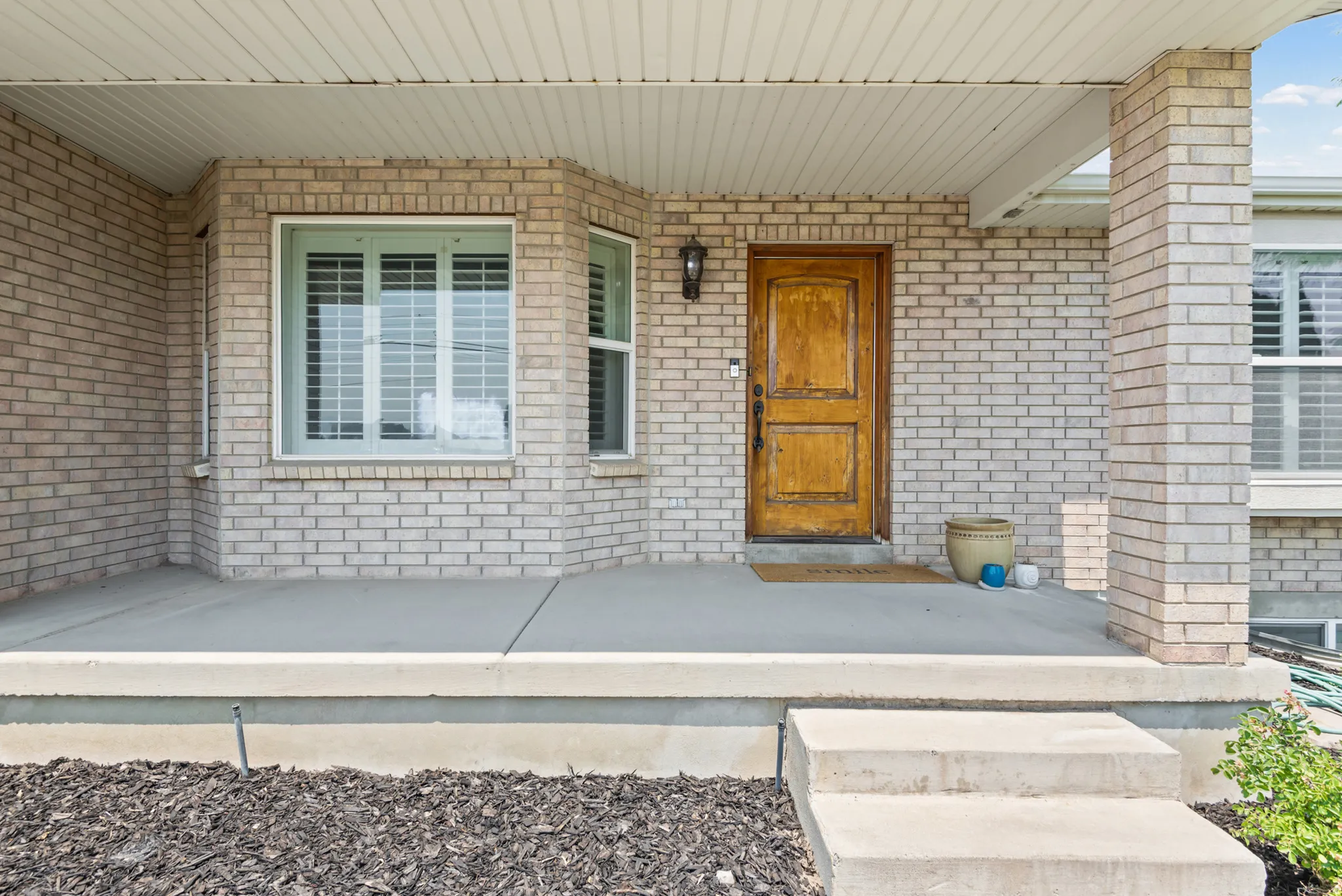 Brick facade featuring a natural wood-finish entry door, an exterior sconce, and a bay window with louvered blinds