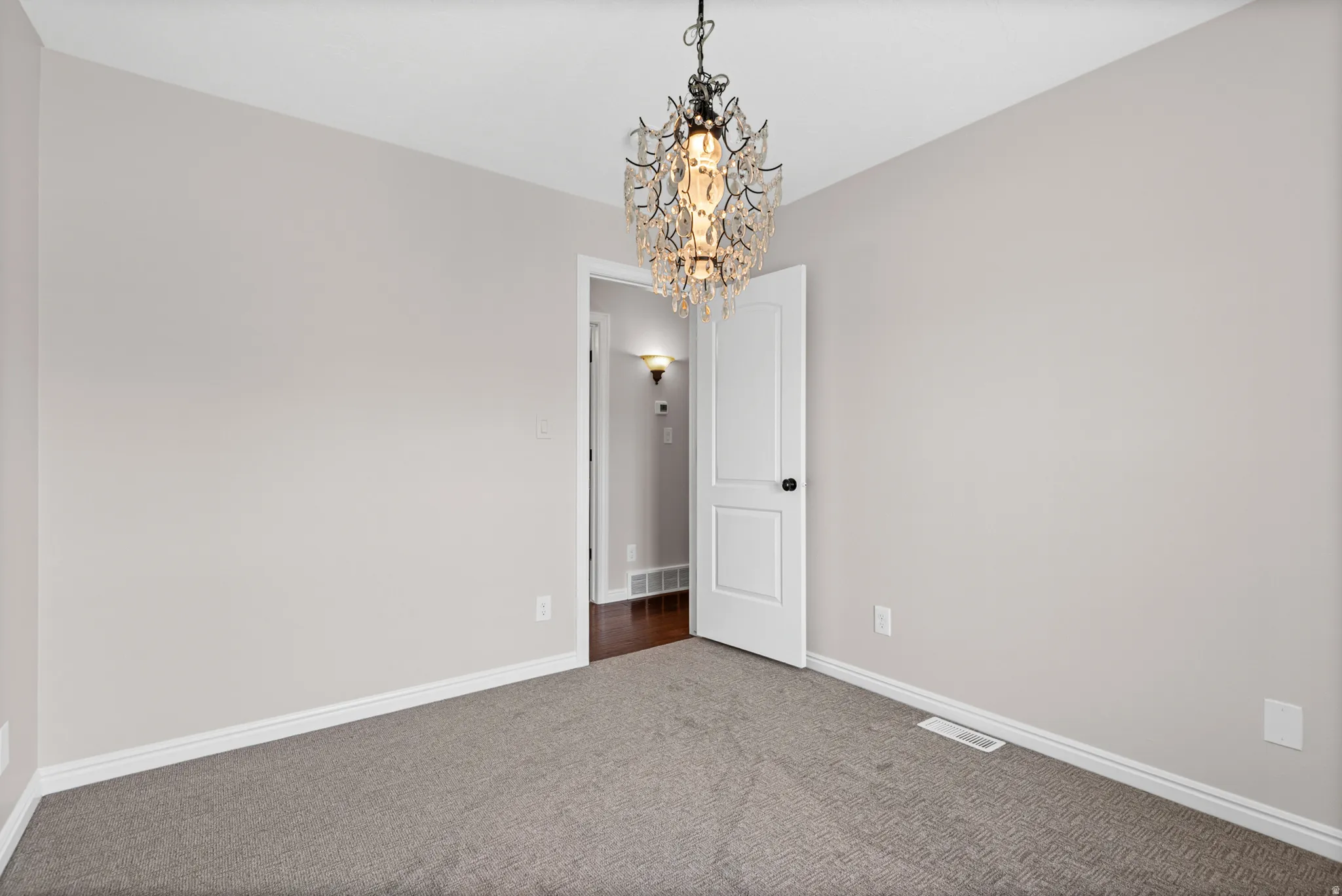 Neutral-toned room featuring a crystal chandelier, light gray walls, white trim, and gray carpeting