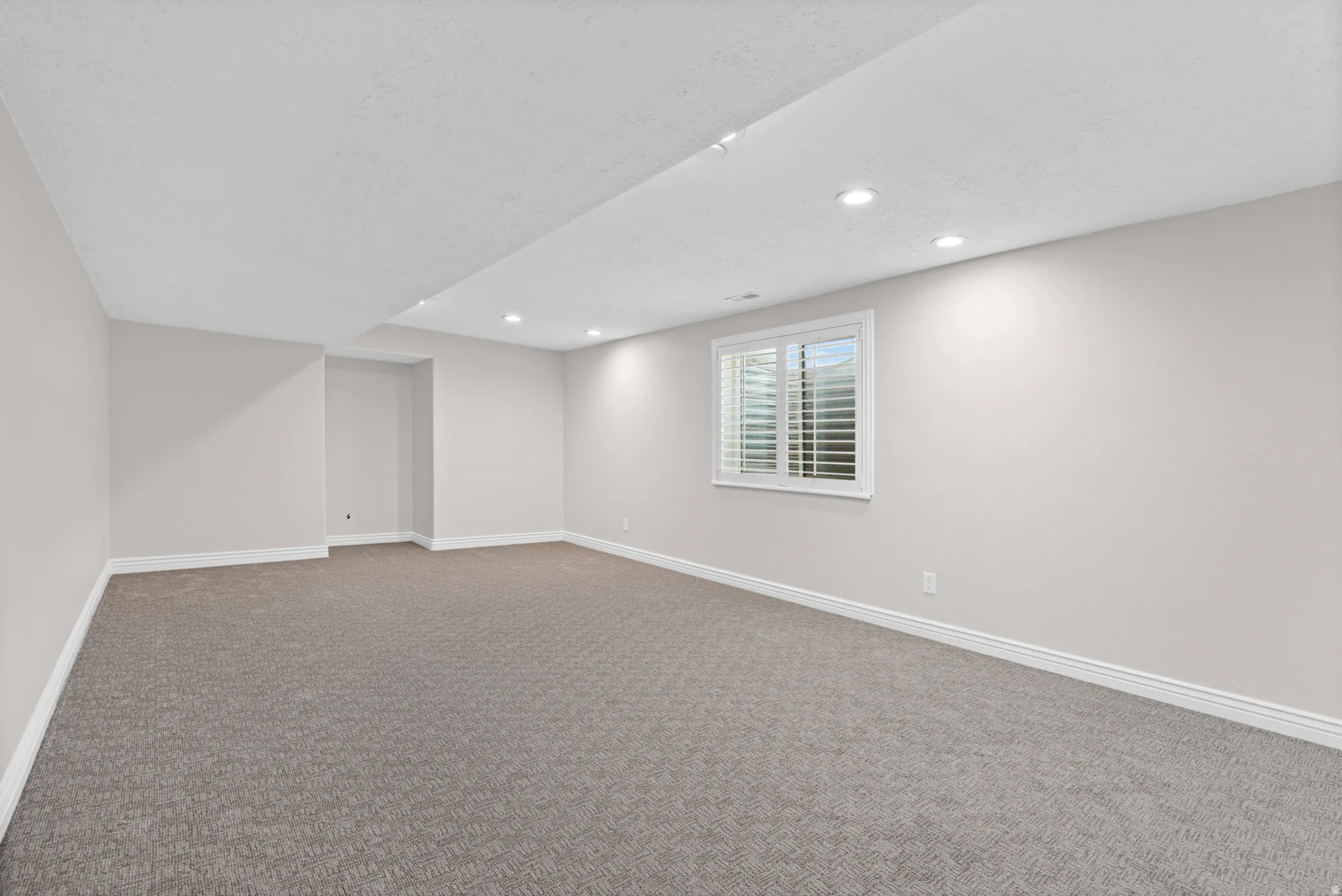 Spacious room featuring neutral carpeting, light-toned walls, and recessed lighting