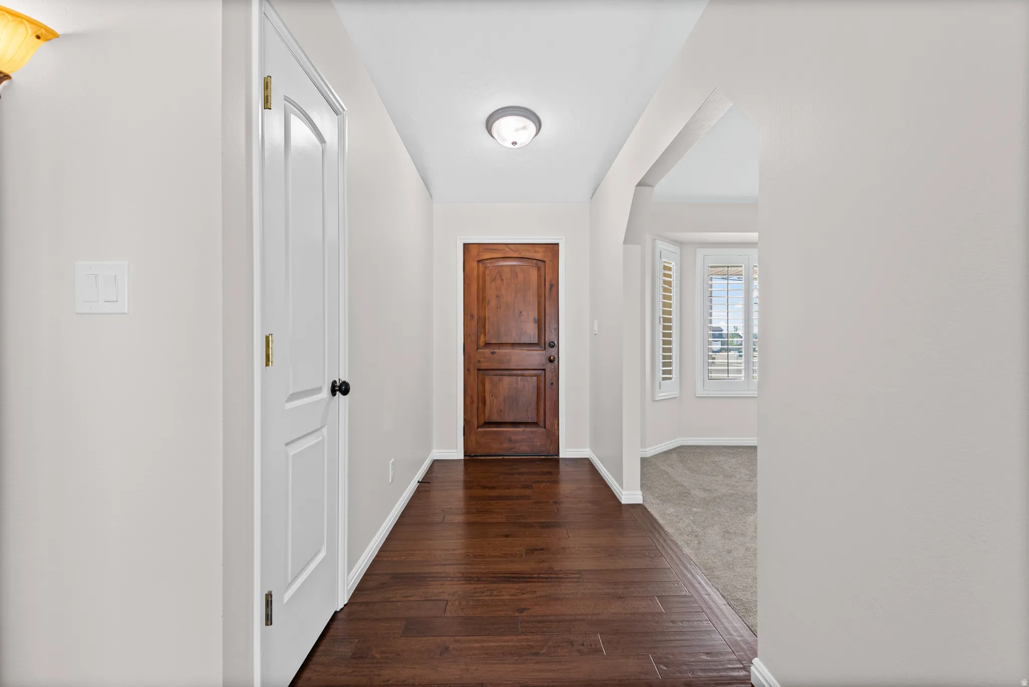 Rich wood-finish flooring extending from the entryway, a paneled front door, and a recessed ceiling light