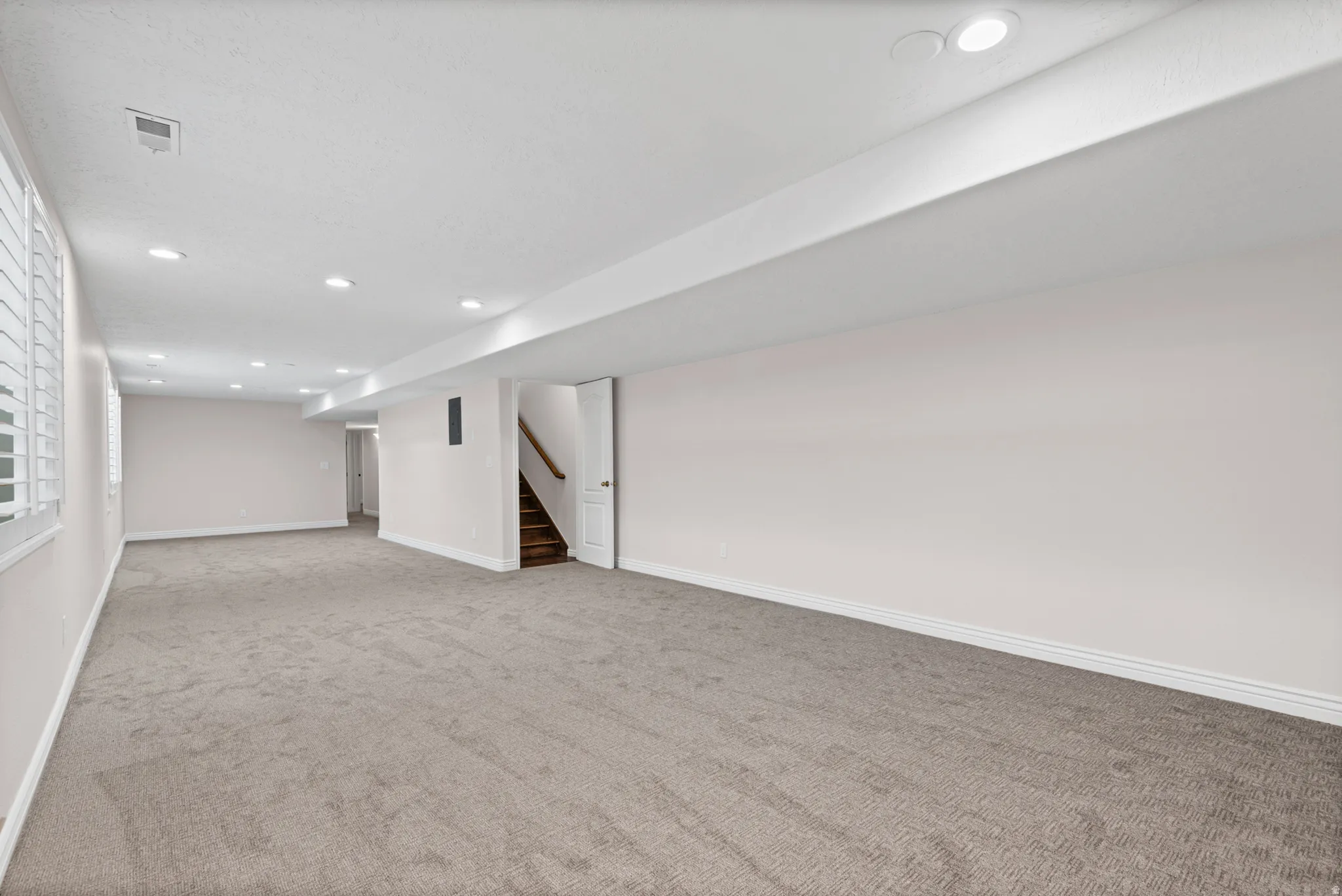 Spacious interior room featuring light gray carpet, recessed lighting, white walls, and white trim