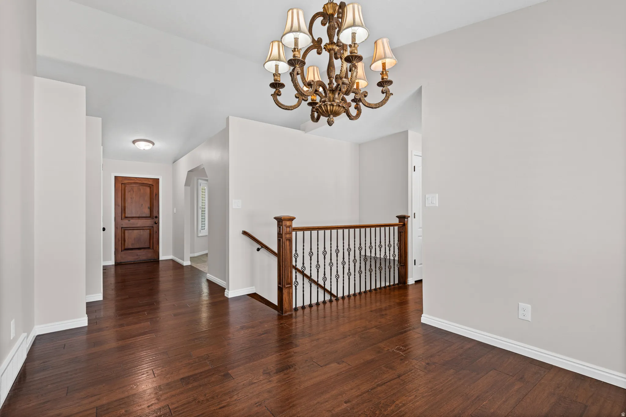 Elegant foyer featuring wood-finish flooring, a decorative chandelier, a detailed wooden entry door, and a staircase with wrought iron balusters and a wood handrail