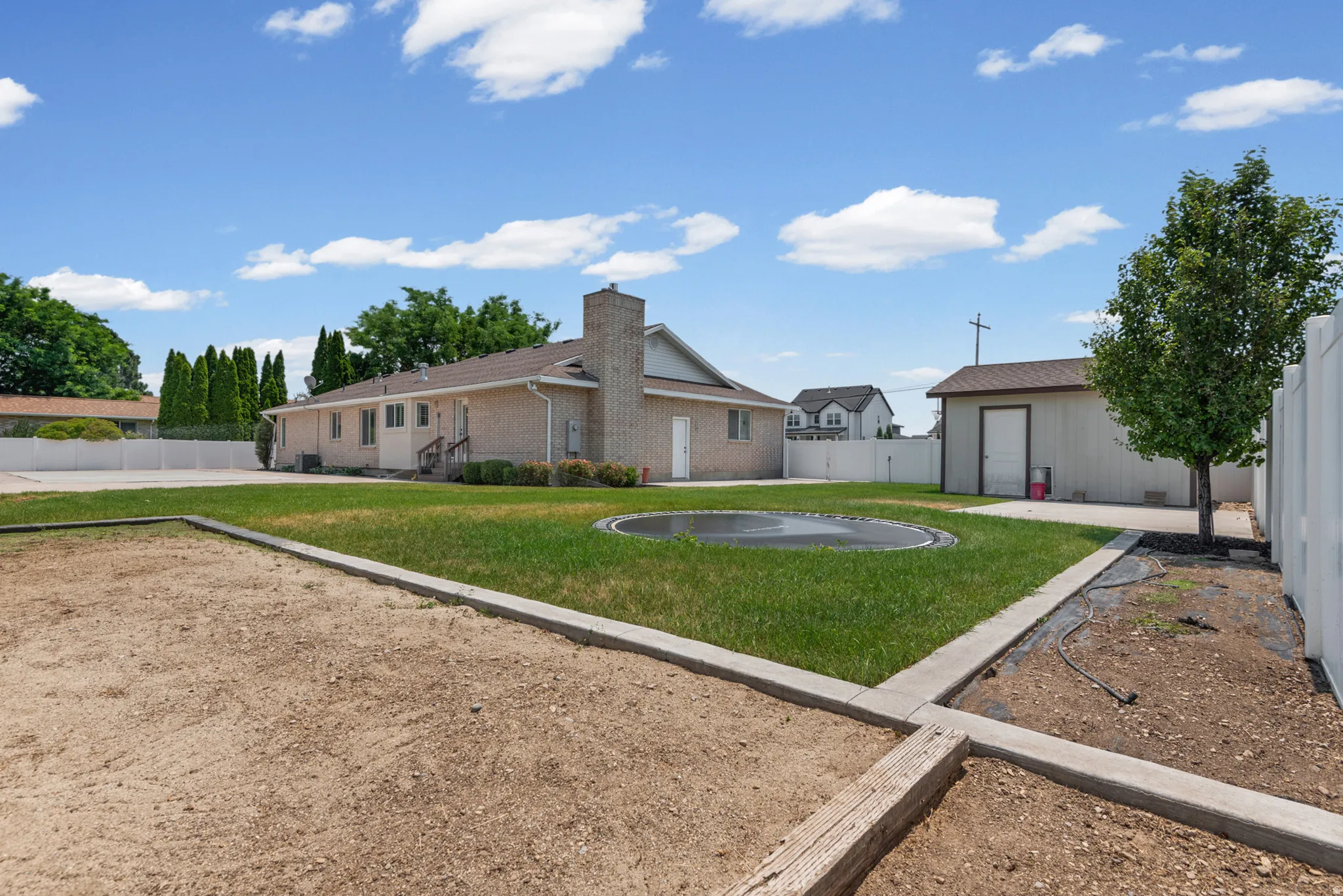 Expansive backyard featuring a manicured lawn, an in-ground trampoline, and a dedicated garden bed