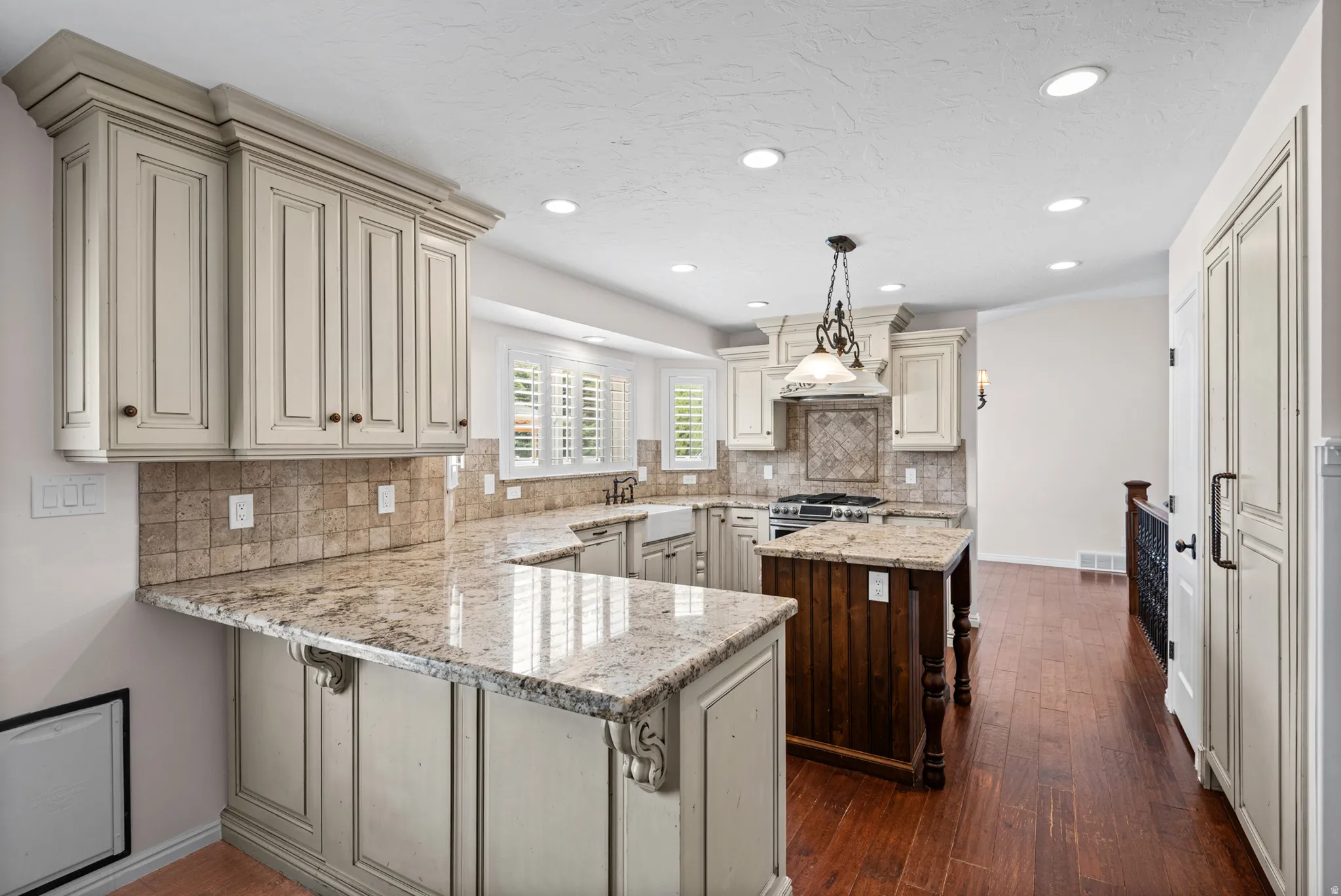 Kitchen featuring U-shaped stone countertops, custom cabinetry with crown molding, a tiled backsplash, and recessed lighting