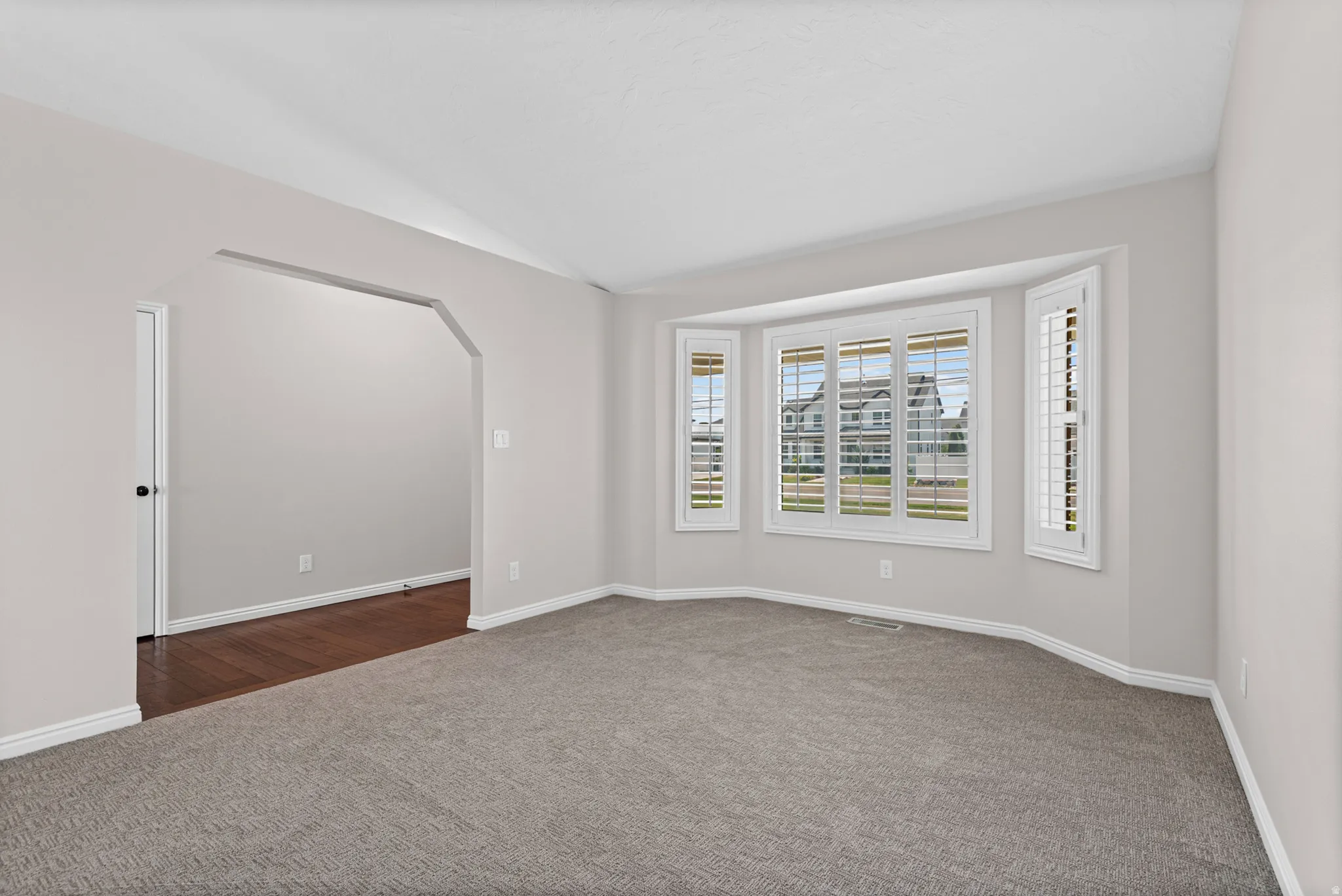 Spacious room with a large bay window featuring white plantation shutters