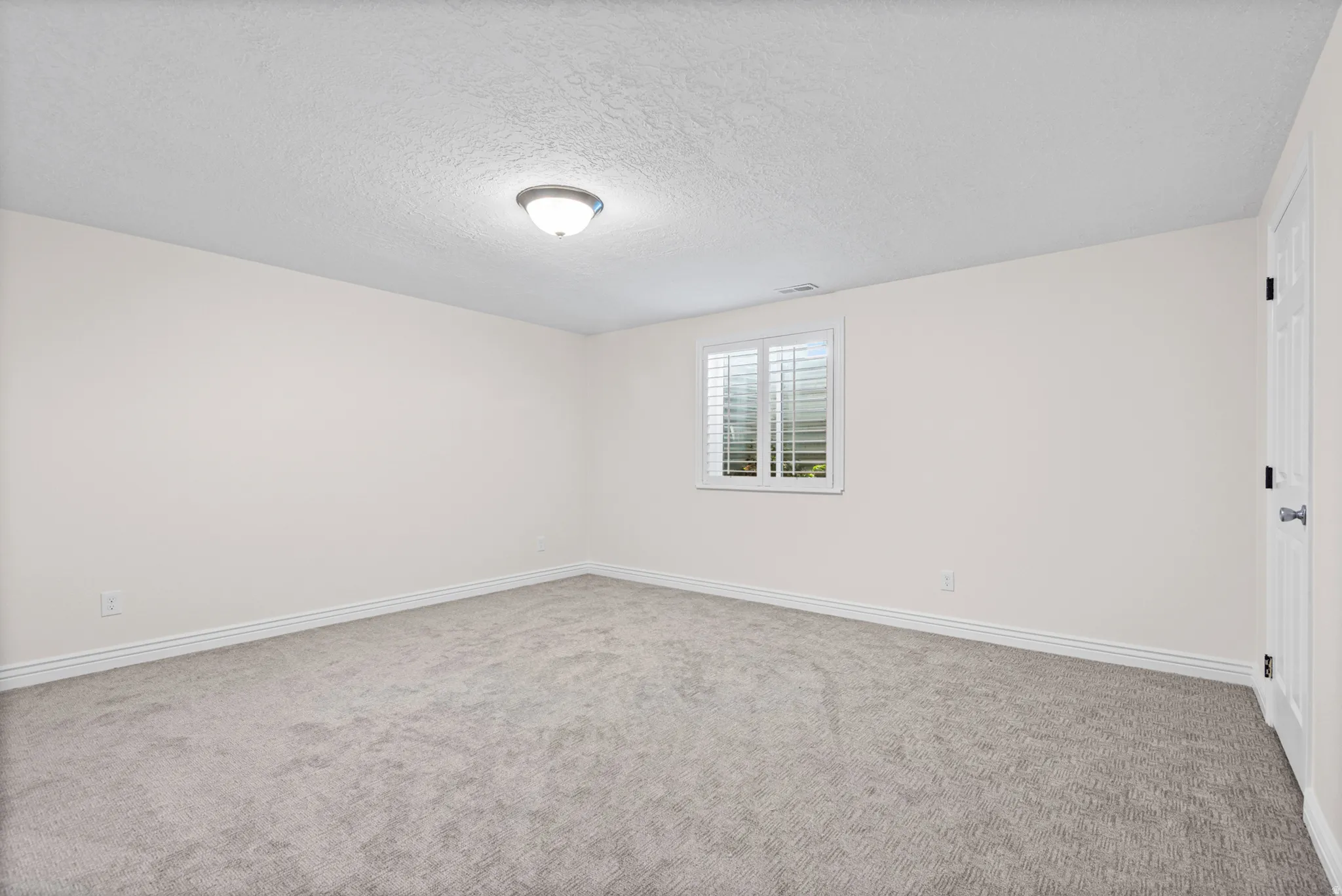 Spacious room featuring neutral carpet flooring, light-toned walls, and a window with white louvered blinds